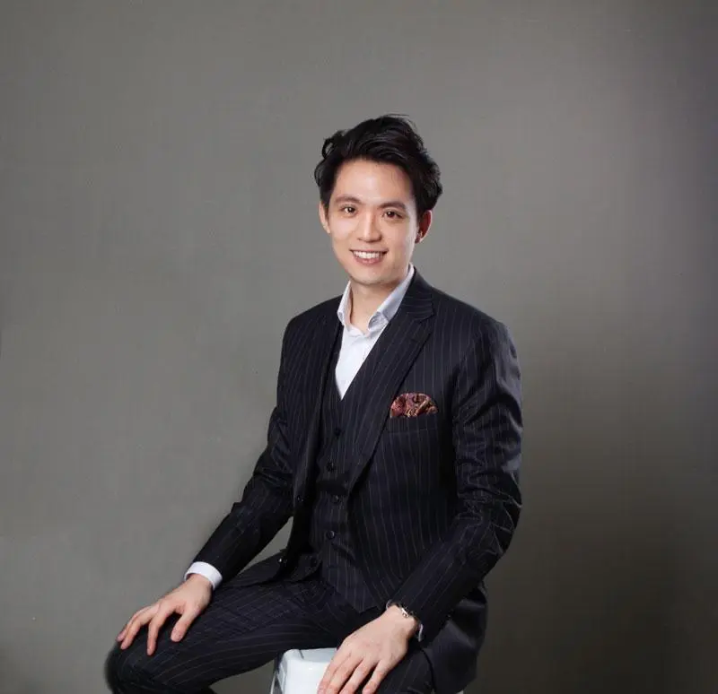 ชายหนุ่มยิ้มกว้างในชุดสูทลายทางสีเข้ม นั่งบนเก้าอี้ พื้นหลังสีเทา ภาพโปรไฟล์ทางการ FUTURE24